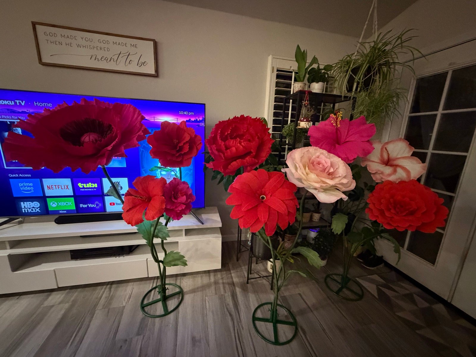 A row of giant paper flowers on green stands: red, pink, peach and white blooms